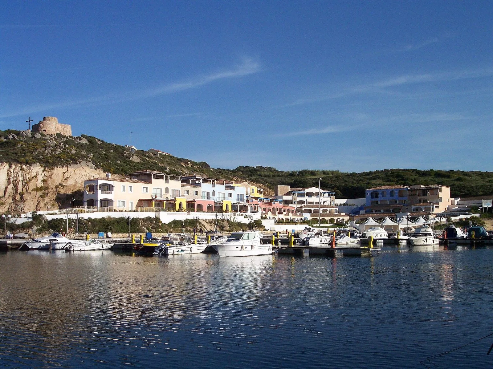 Il porto di Santa Teresa Gallura con barche ormeggiate, case colorate sul lungomare e una torre sulla collina