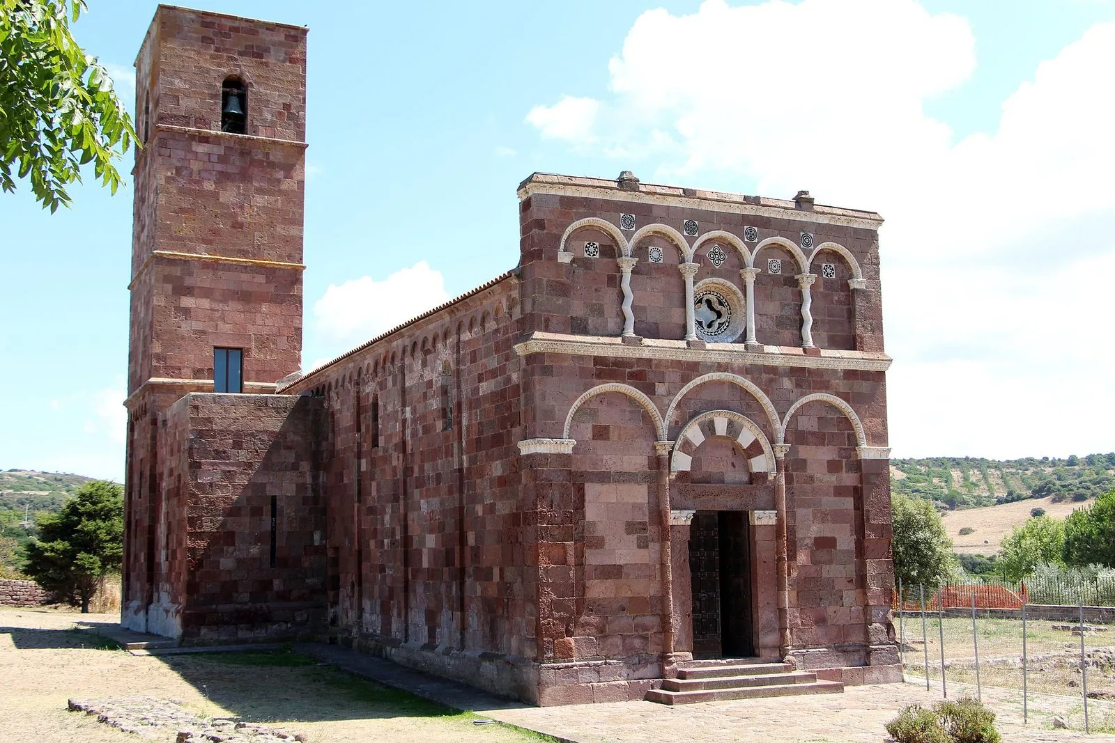 Facciata in pietra rossastra e chiara della basilica di Nostra Signora di Tergu con il campanile
