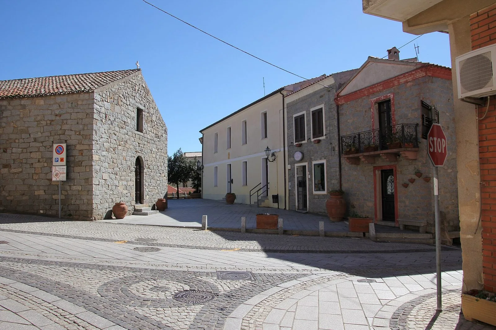 Una piazza del centro di Trinità d'Agultu con edifici e una chiesa in pietra di granito